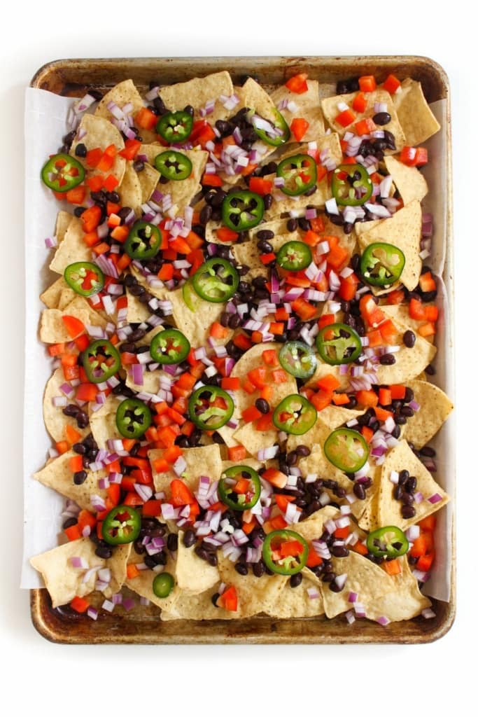 tortilla chips with diced bell peppers, black beans, jalapeños, and other veggies on a sheet pan