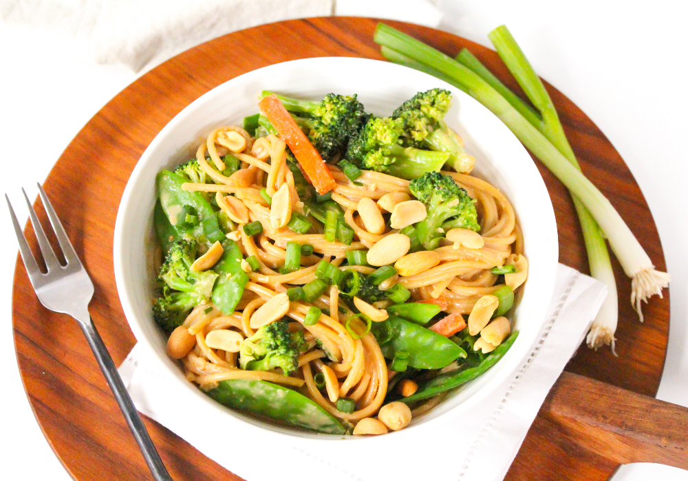 peanut butter pasta with veggies in a white bowl on a wooden platter